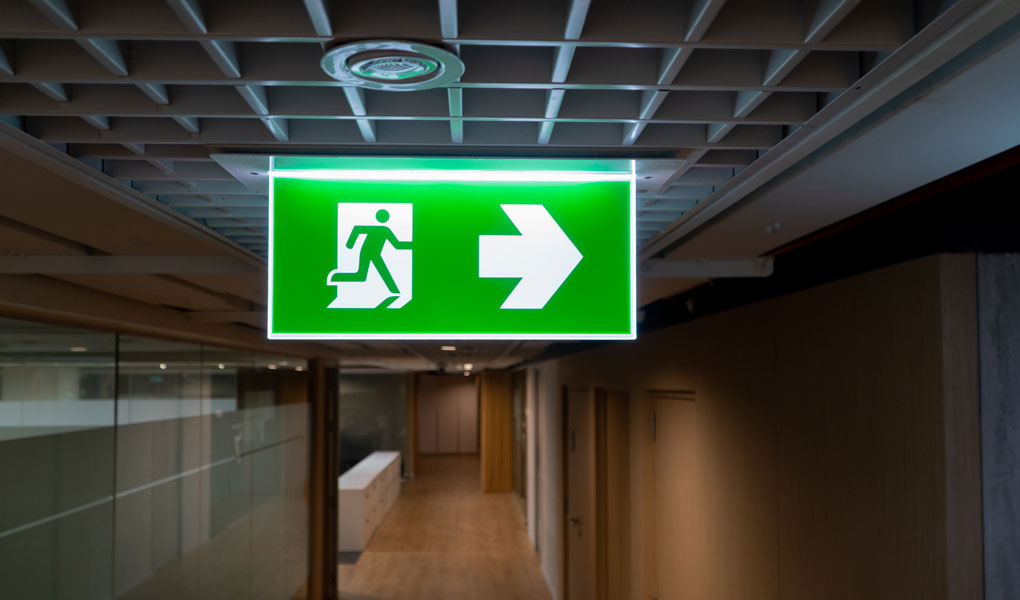 Green fire escape sign hang on the ceiling in the office. 
